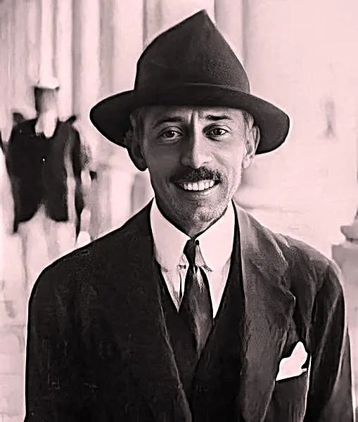 Fotografia de Alberto Santos Dumont sorrindo, de chapéu de feltro, terno e gravata.